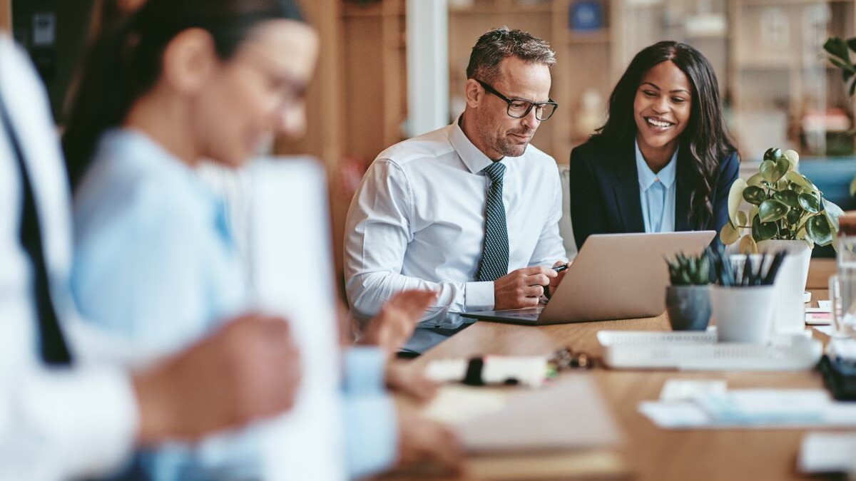 Two smiling diverse businesspeople using a laptop together at work